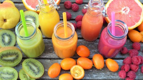 Various smoothies in jars on table next to assorted fruits